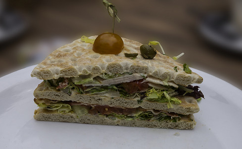 模糊背景图摄影照片_面包上放着健康三明治的白盘子，上面放着生菜番茄和其他东西