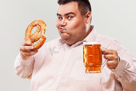 慕尼黑啤酒节上的年轻胖子，喝着啤酒，吃着白色背景中突显的椒盐卷饼。