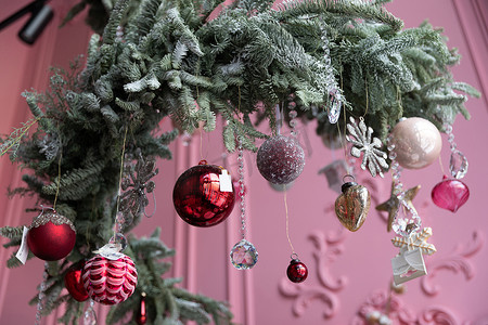 天花板上悬挂着天然松针和冷杉的时尚圣诞树布置，在粉色墙壁的背景下装饰着圣诞装饰
