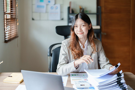 财务报表摄影照片_财务、规划、营销和会计，亚洲员工在工作中使用文件和笔记本电脑检查财务报表的肖像