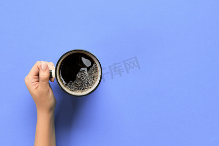 简约紫色背景摄影照片_高角度的女人手拿着紫色背景简约风格的咖啡杯。