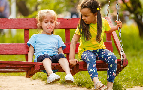 孩子生气摄影照片_伤心的女婴在公园里哭着，秋千坏了。