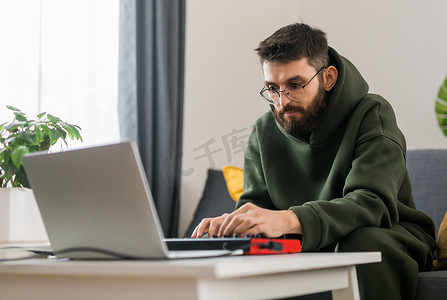 男子在家庭工作室的笔记本电脑上用便携式 midi 键盘录制电子音乐曲目。