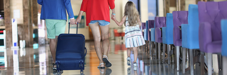 在机场或酒店行走时带手提箱的家庭后视图