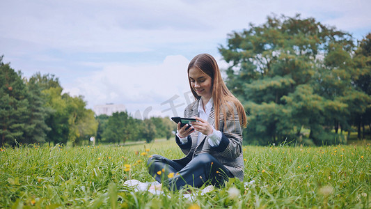 一个小女孩坐在公园的草地上，用手机和银行卡购物。