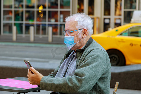 在纽约大流行病旅行期间，老人戴着手机走在街上，以保护自己免受冠状病毒感染