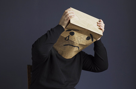 暴风哭泣摄影照片_悲伤的男人头上顶着一个袋子，画着哭泣的表情符号。