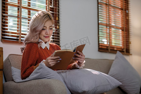 迷人的年轻亚洲女性坐在简约而舒适的客厅里，享受着读书的乐趣。