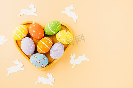 剪鸡蛋摄影照片_头顶的复活节彩蛋，兔纸剪成形状的心，与柔和的背景隔离