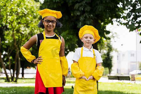 身着黄色厨师帽和围裙的非洲黑人和白人厨师儿童的多种族朋友之间的交流，一起讨论和玩乐。