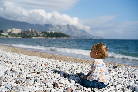 孩子坐在海边的卵石滩上。