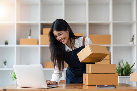 自由职业亚洲女性的初创 SME 小企业企业家使用笔记本电脑和盒子在线接收和查看订单，准备打包销售给客户，在线中小企业商业理念