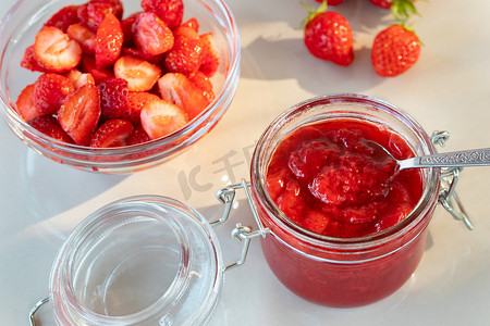 玻璃瓶装草莓酱，准备装罐，桌上碗里放新鲜草莓