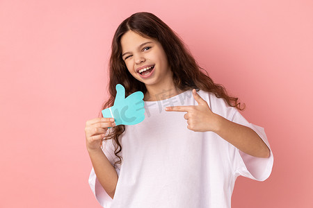 快乐满意的可爱小女孩拿着并指着喜欢或竖起大拇指的纸形标志。