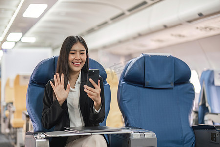 电话视频摄影照片_在飞机飞行期间，年轻女子坐在靠近窗户的飞机座位上，进行电话视频通话