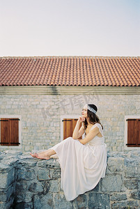 新娘坐在一座古建筑的石墙上，手托着下巴