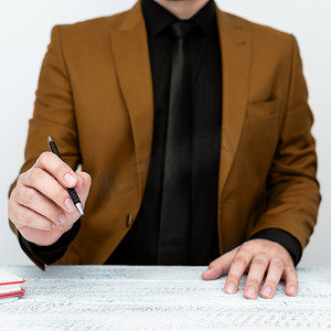穿着棕色西装的男模特坐在白桌旁，用笔指着重要信息。