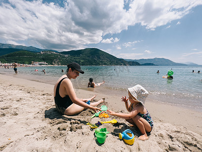 妈妈和一个小女孩在海边用塑料模具塑造沙人