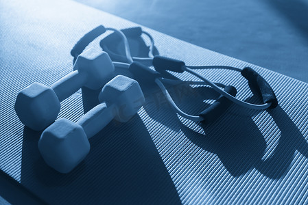 在健身俱乐部用橡胶扩张器和两个哑铃放置在地板上的垫子