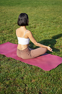 做瑜伽、坐在健身垫上和在绿色草坪上冥想的女性剪影的后视图