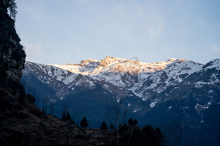 阳光照耀着远处覆盖着雪的山峰，马纳里的前景是树木覆盖的山脉