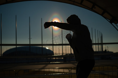 日落时分，一名身穿运动衫的男子在体育场进行拳击训练。