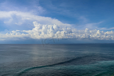 平静的海面和蓝天从船的侧面看去，船头波浪尾迹和地平线上的积雨云。