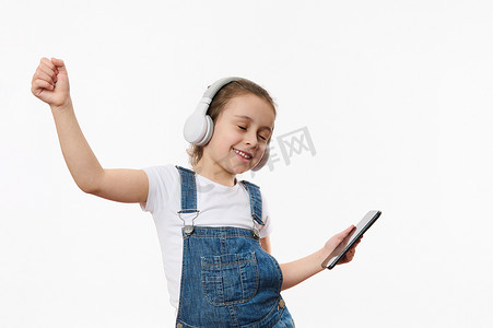 穿着蓝色牛仔布的可爱女婴，拿着智能手机，一边用立体声耳机听音乐一边跳舞