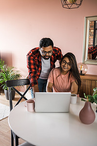 技术远程工作和生活方式概念 — 戴眼镜、带笔记本电脑在家办公室工作的快乐印度男女