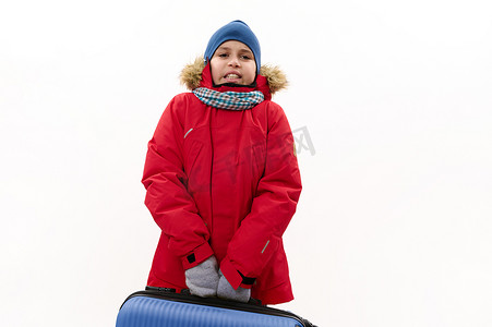 中东十几岁的男孩，穿着带毛皮罩的红色皮大衣，拿着一个蓝色手提箱，在白色背景中突显