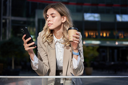 穿着西装、喝咖啡外卖并使用手机应用程序的时尚企业女性