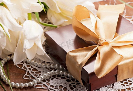 礼物金色丝带摄影照片_一条金色丝带的礼物，一束带绿叶的白色郁金香。