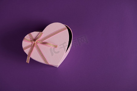 半开放心形粉红色礼品盒的顶视图，紫色背景上系着蝴蝶结。