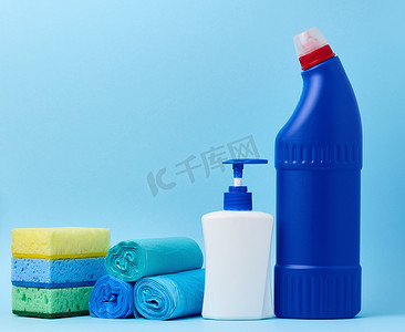 蓝色背景上带分配器和垃圾袋的白色塑料瓶、海绵和带洗涤剂的蓝色瓶子