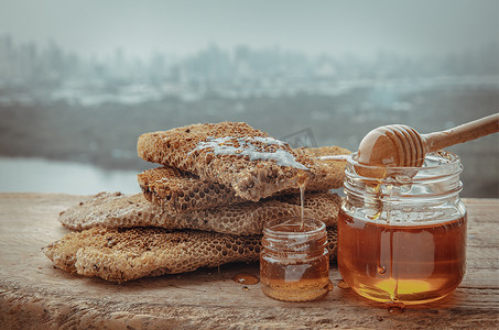 美味的蜂蜜从玻璃罐上的新鲜蜂窝滴下来，旧木桌上有木制蜂蜜勺子。