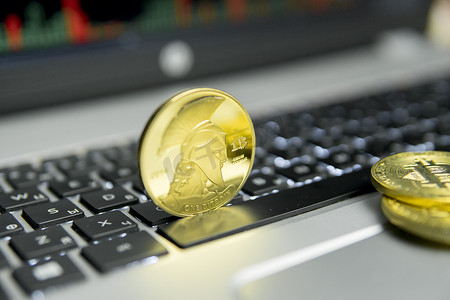 金泰坦比特币与金币躺在笔记本电脑的银色键盘上，屏幕上的图表图表作为背景。