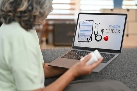 评估诊断摄影照片_成熟的女性患者在笔记本电脑上在线检查或检查她的健康状况。