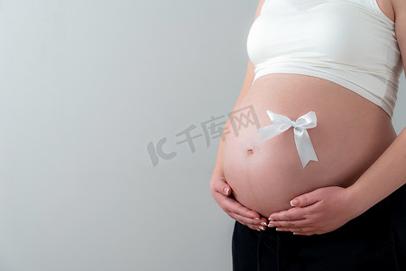 怀孕后期美丽的女性腹部作为带白色蝴蝶结的礼物