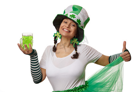 狂欢节服装摄影照片_穿着妖精狂欢节服装的积极可爱的女人，拿着一杯绿色啤酒，微笑着庆祝圣帕特里克节