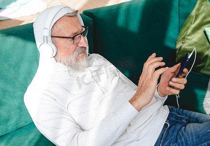 在家用耳机在智能手机上听音乐的老年老人特写肖像 — 活跃的老年人概念