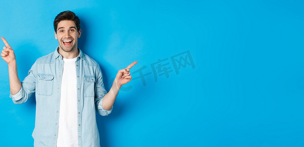 家电促销海报摄影照片_快乐的成年男子微笑着，手指向侧面，展示左右促销横幅，站在蓝色背景下