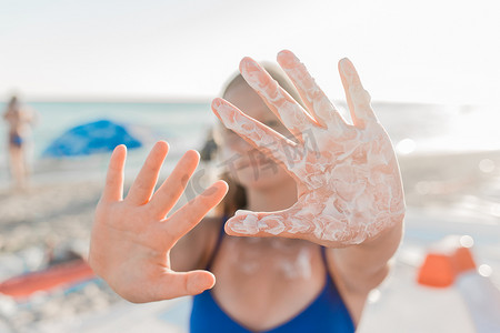 一位年轻的欧洲少女在海滩的背景下，手掌上涂着防晒霜和防晒霜，双臂向前伸展