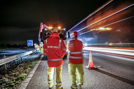 道路指示牌摄影照片_夜间高速公路上的工人与车辆驶过