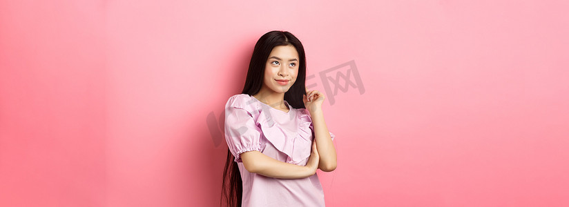 美丽的亚洲女人微笑着望向一边，穿着粉色浪漫背景中的裙子