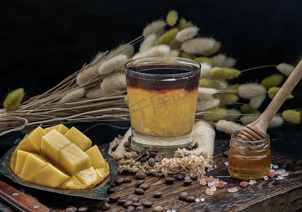 冰芒果摄影照片_一杯冰镇热带芒果冰沙混合浓缩咖啡和蜂蜜放在木菜板上。