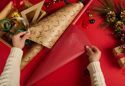 端午节礼摄影照片_女人手的顶部视图，推出红色礼品纸和鹿图案，包装，包装圣诞礼物。