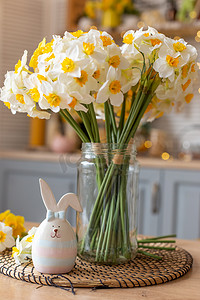 厨房的桌子上放着一个可爱的兔子陶瓷雕像，旁边是一个插着水仙花的玻璃花瓶。