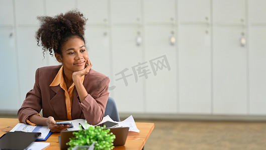 坐着的会计摄影照片_冷静的女商人坐在工作场所，望着窗外思考投资策略或项目成功