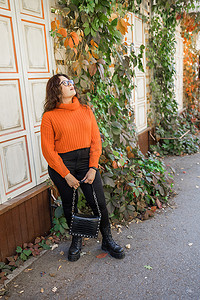 时尚橙色摄影照片_秋季肖像的迷人沉思年轻女子在时尚眼镜在针织时尚橙色毛衣在叶子的背景。