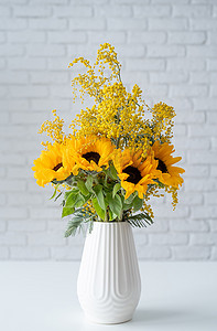 白砖墙背景白色陶瓷花瓶中含羞草和向日葵的开花，有文字空间